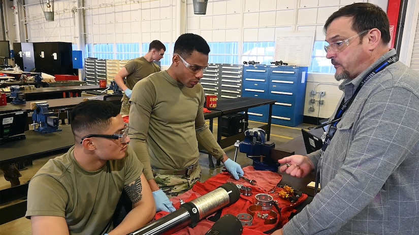 U.S. Army Pvt. Jeremy Vitales, left, and Pvt. Kristopher Powell, 1st Battalion, 210th Aviation Regiment, 15H students, perform simulated maintenance on aircraft hydraulic components while Mr. Trevor Johnstin, 1st Battalion, 210th Aviation Regiment, instructor, monitors their progress during the aircraft pneudraulics repairer course at Joint Base Langley-Eustis, Virginia, January 24, 2023. During the course, students will learn to diagnose and troubleshoot mechanical components associated with pneudraulic systems in aircraft. (U.S. Air Force photo by Abraham Essenmacher)