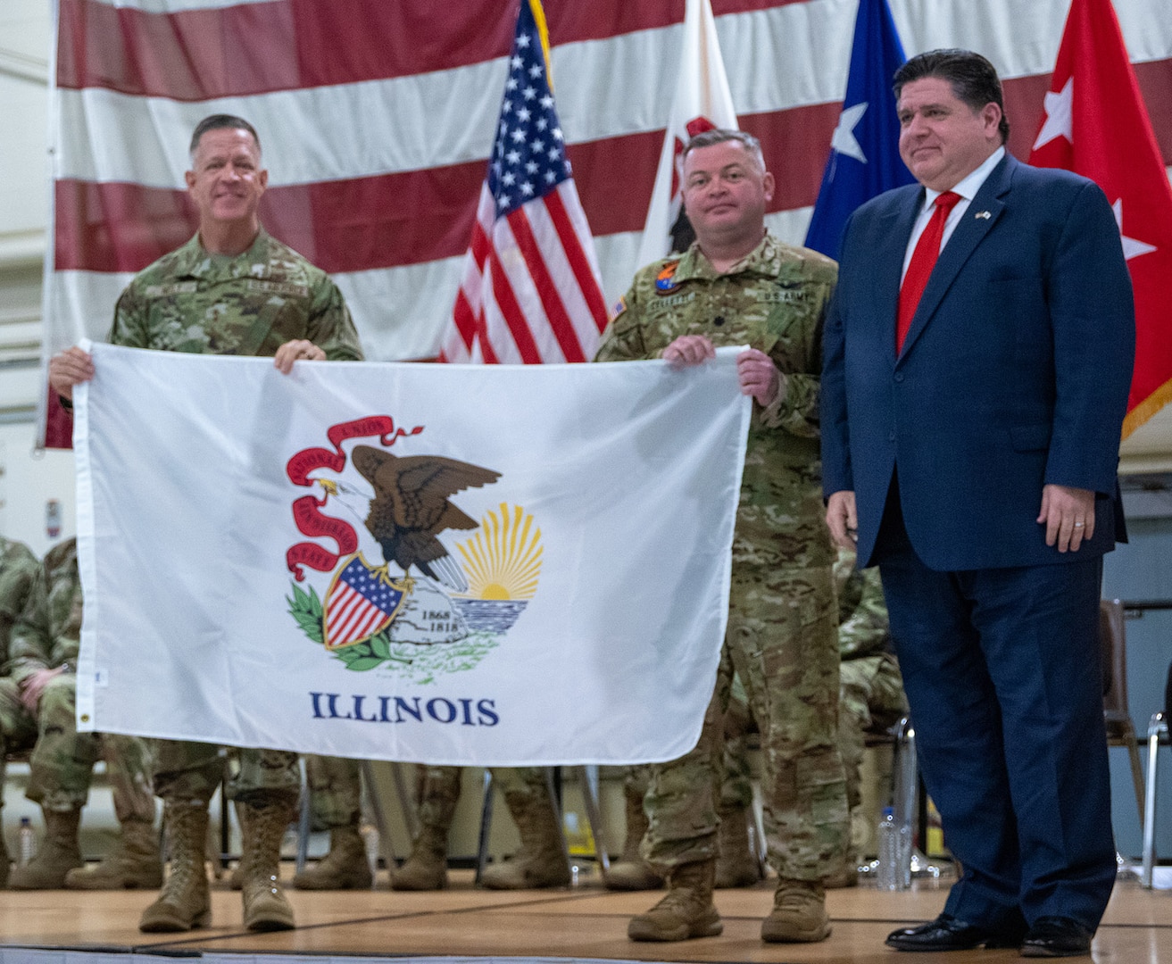Illinois Gov. JB Pritzker, right, and Maj. Gen. Rodney Boyd, the Adjutant General of Illinois and Commander of the Illinois National Guard, presents Lt. Col. Jason Celletti, commander, 1st Assault Helicopter Battalion, 106th Aviation Regiment, with an Illinois state flag during the mobilization ceremony Feb. 7 at the 182nd Airlift Wing, Peoria. The flag will travel with the unit as they deploy to the U.S. Central Command area of responsibility.