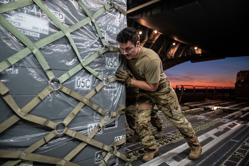 A military member pushes a pallet in the rear of an aircraft.