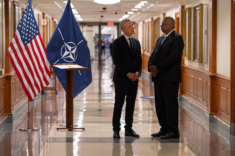 Two men speak in a hallway.