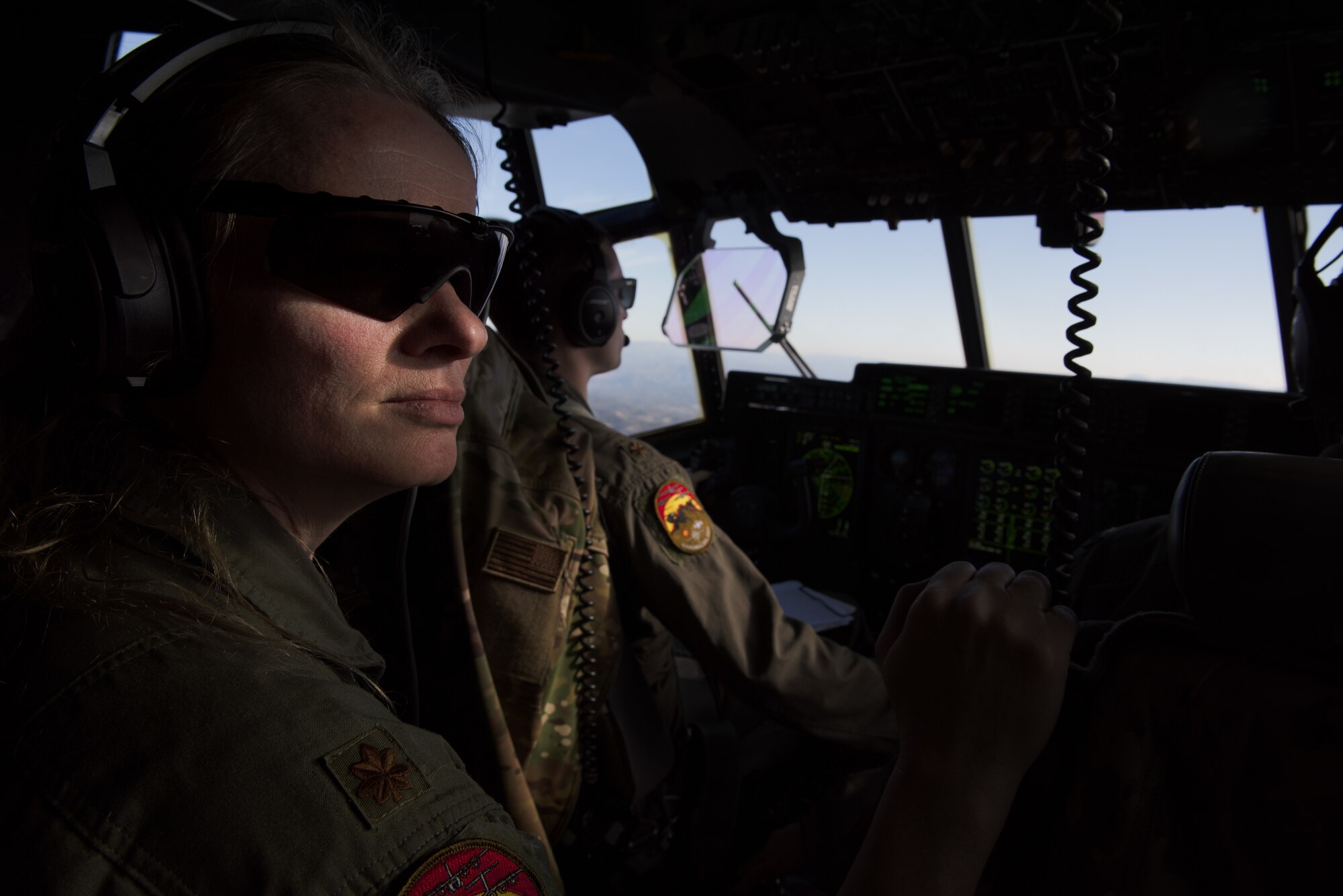 A woman looks towards the camera while sitting in the cockpit of a C-130J