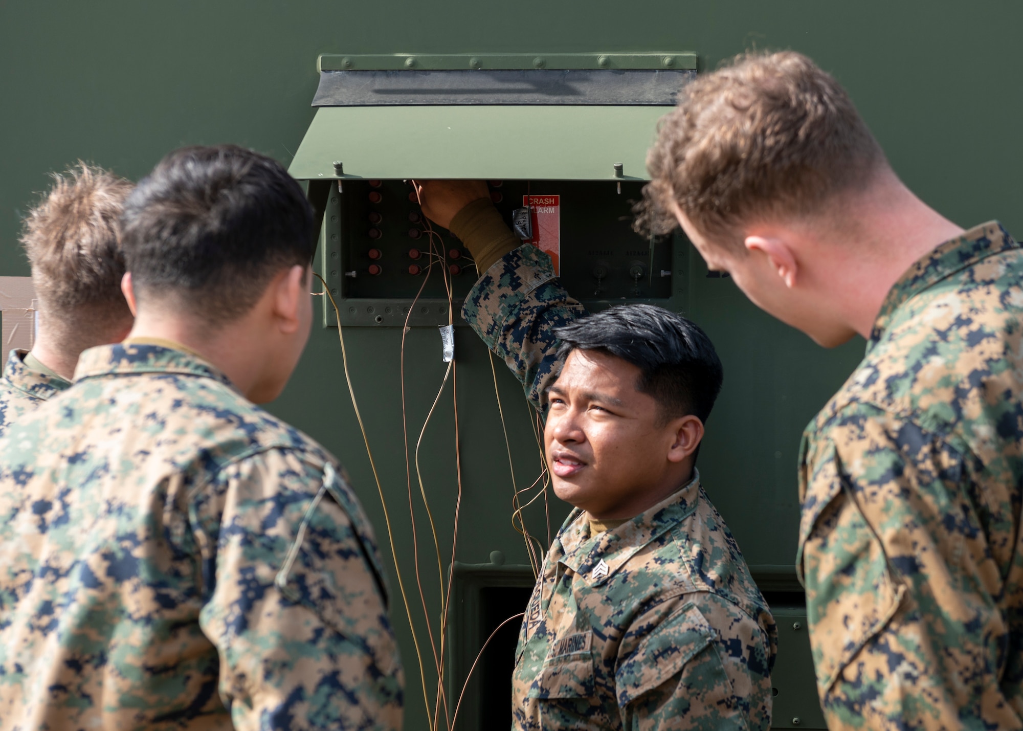 four marines stand around an open electrical panel talking