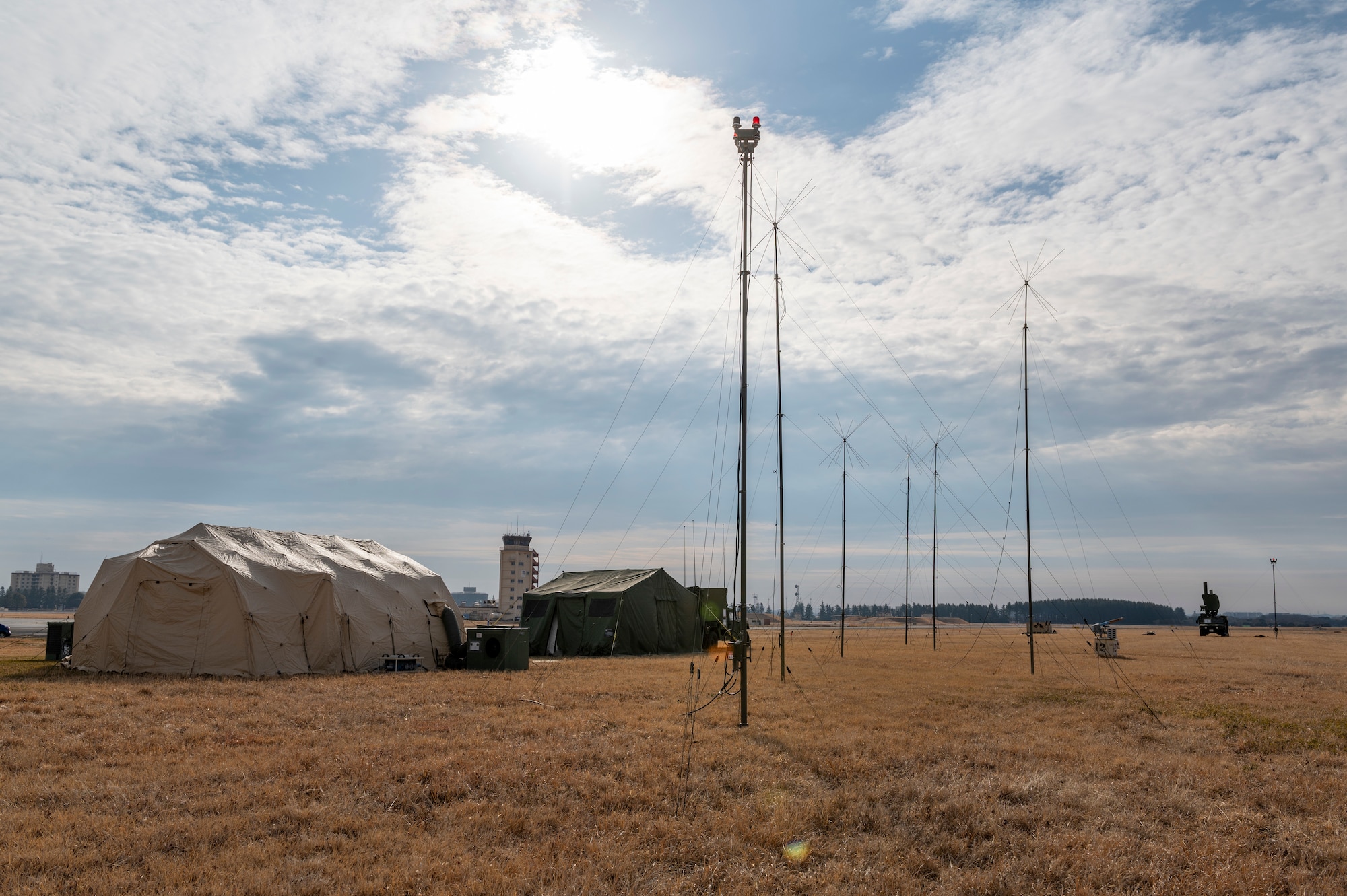 A tower looms over a tent, two military jeeps and several antennas stuck into the ground nearby.