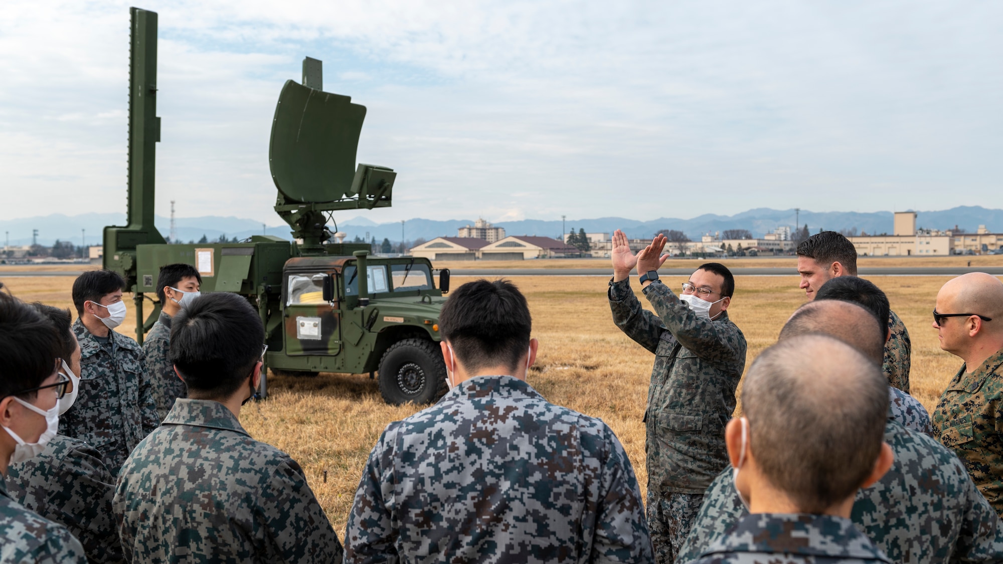 Japanese air force members crowd around a military jeep with a radar dish on top