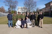 Twenty people, a combination of marines, sailors, civilians and one bulldog posing for a group photo on a grassy parade ground.