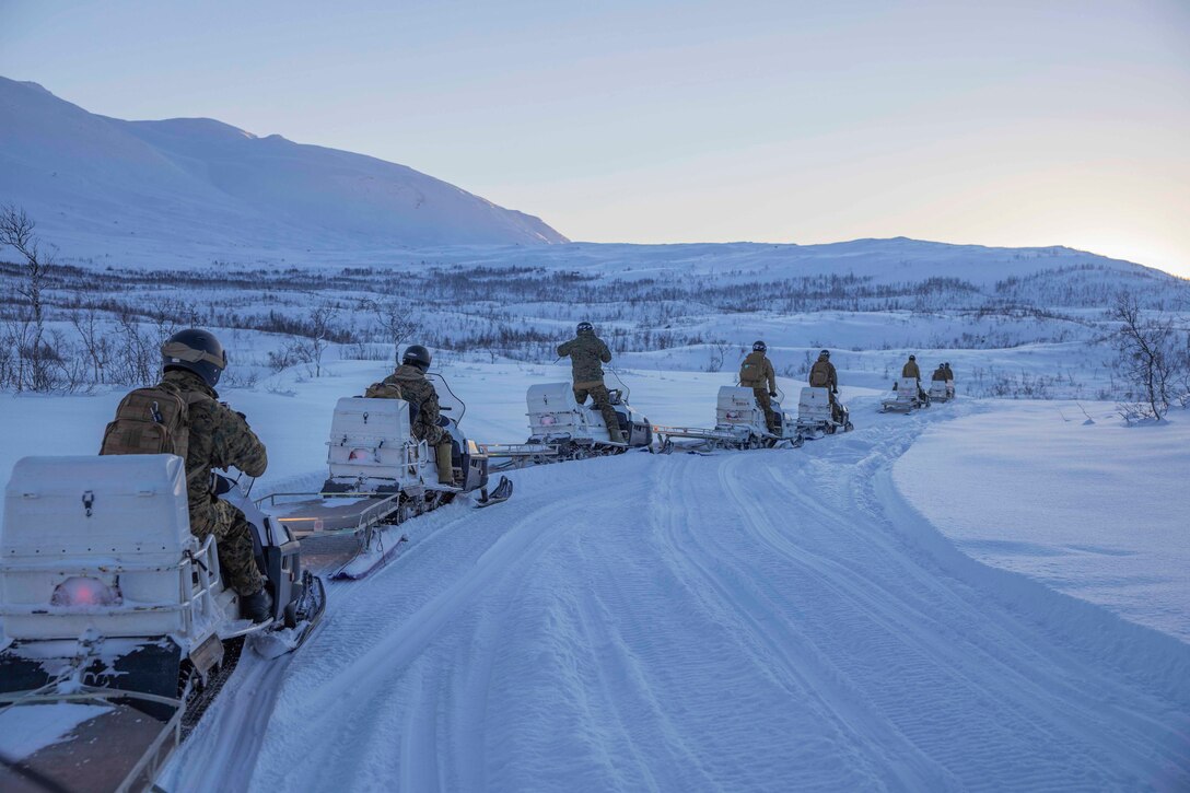 Marines lined up on snowmobiles conduct a convoy .