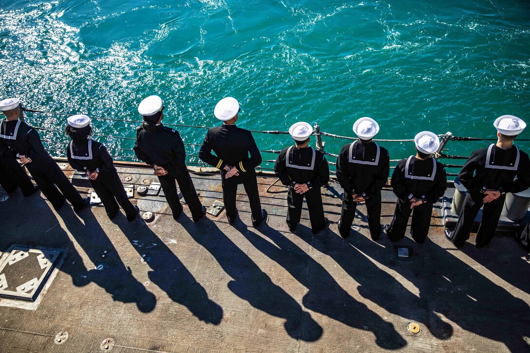Sailors stand side by side while manning the rails.