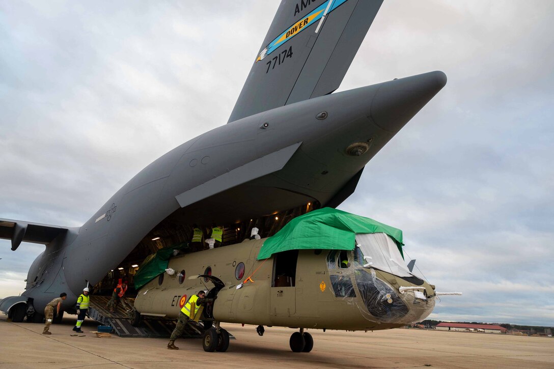 Service members unload a helicopter from a large aircraft.