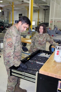 Two Airmen in workshop, male Airmen looking for tool in drawer.