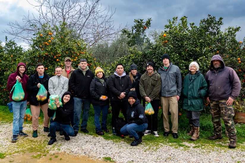 A group of sailors display bags of oranges as they pose for a picture.