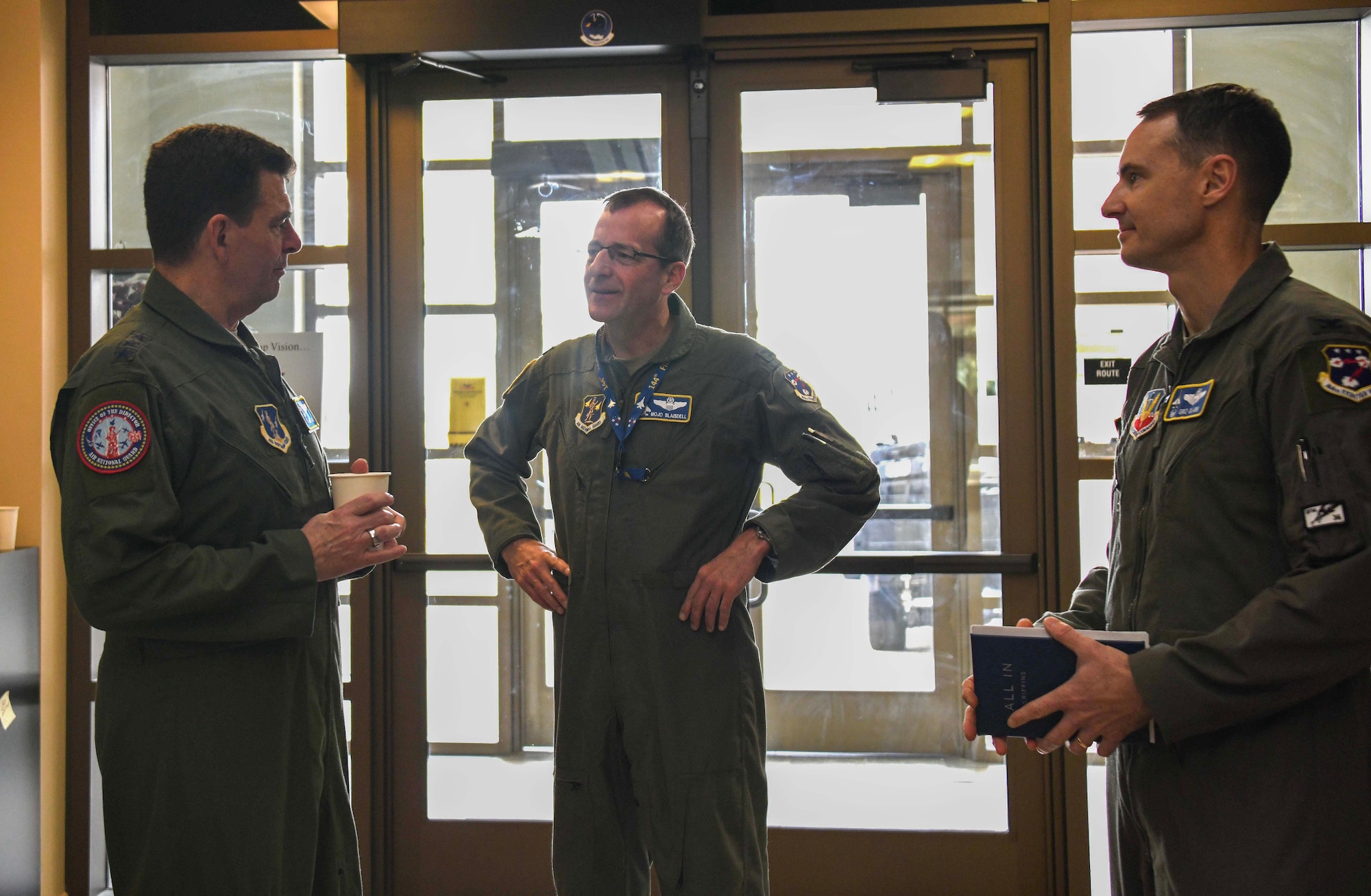 three men in military flight suits speak to each other