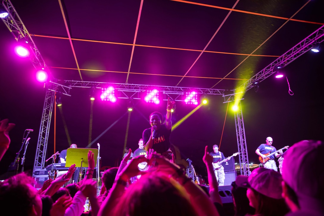 A soldier sings during a performance and points to the audience from the pink-lit stage.