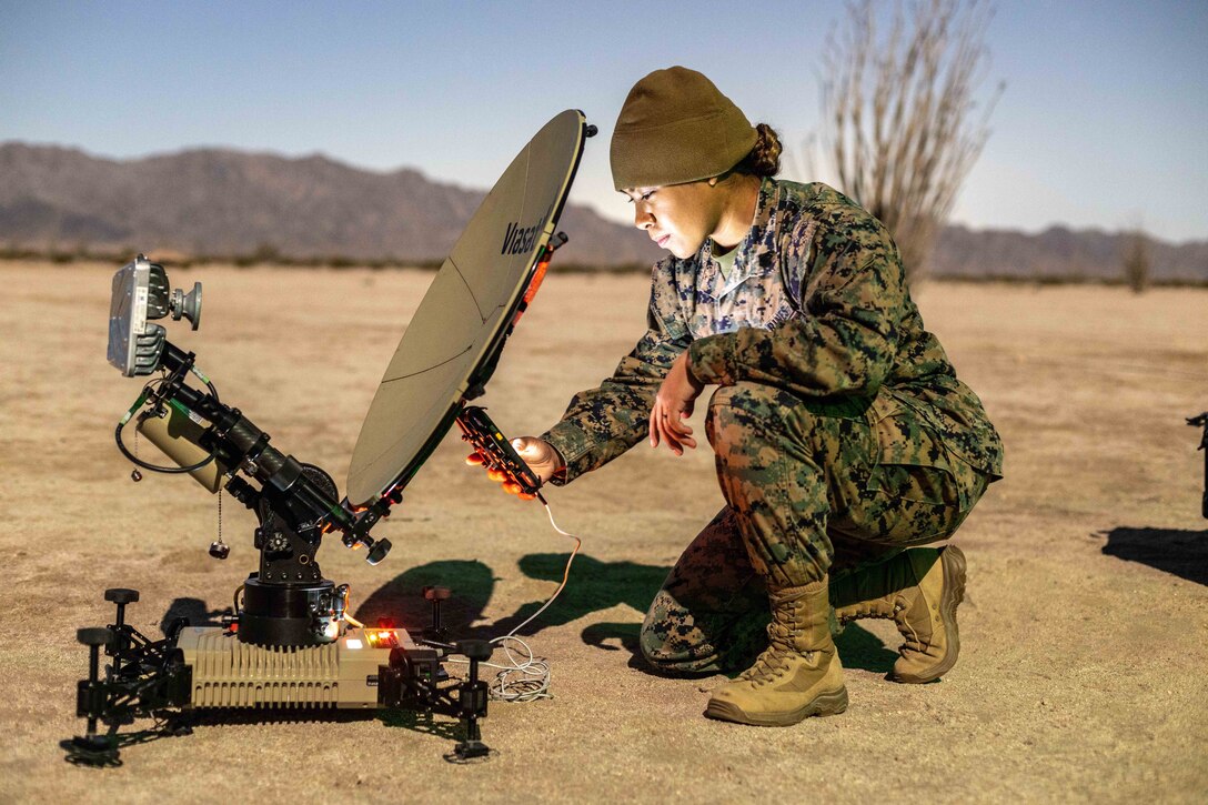 A service member kneels to set up a satellite communications terminal in the Arizona desert.