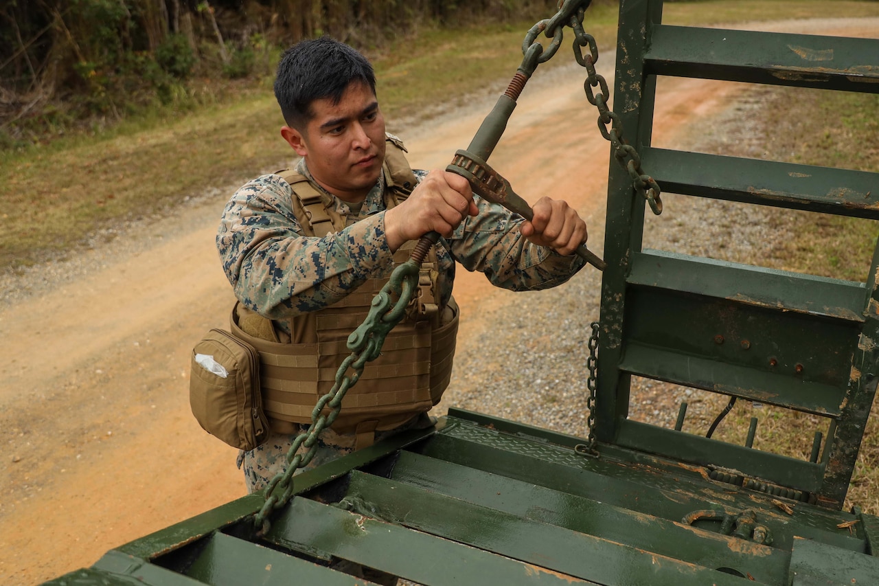 A man in military uniform holds the safety chain of a tow trailer.