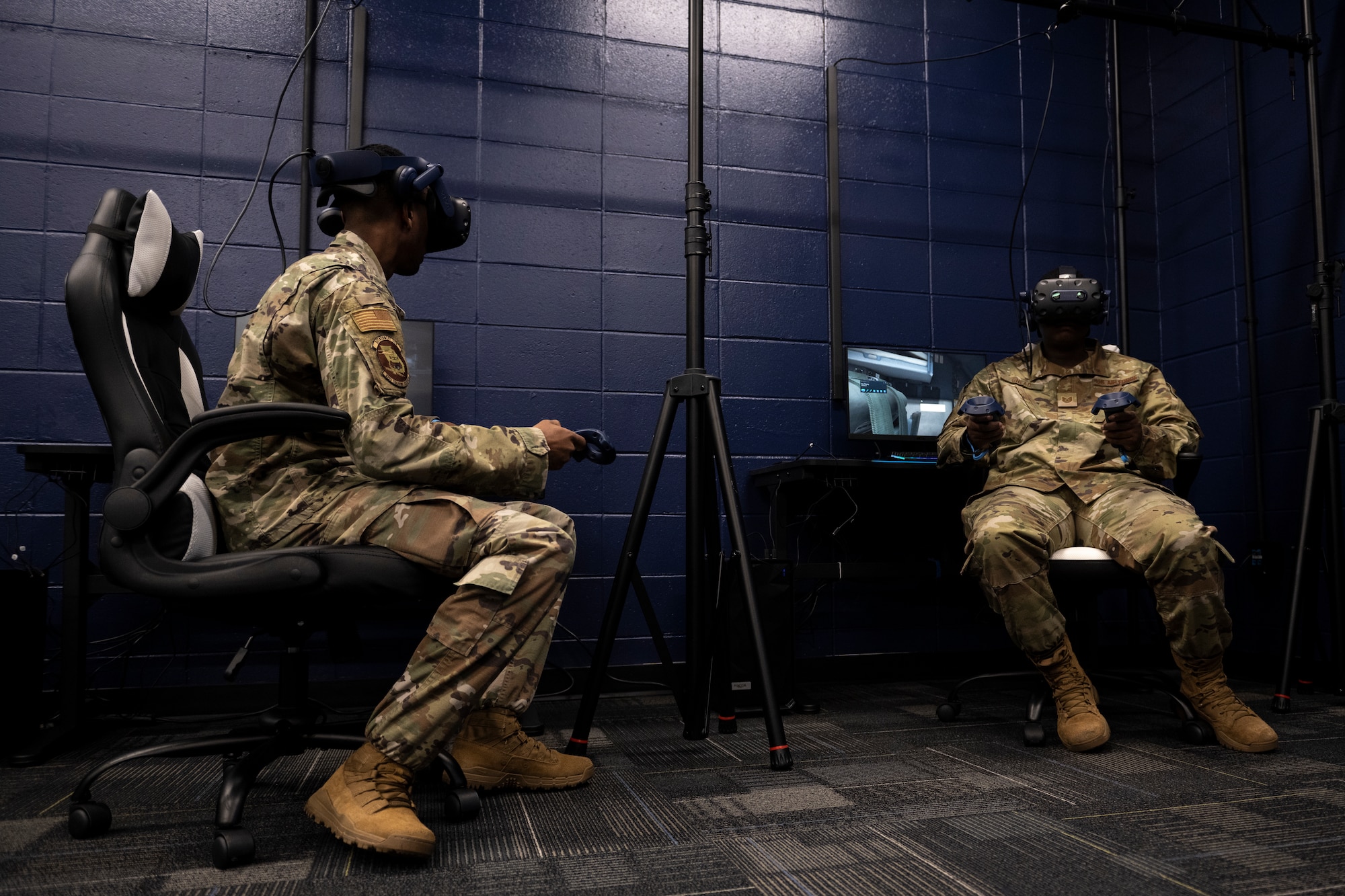 A photo of two Airmen sitting down in chairs with VR headsets on.