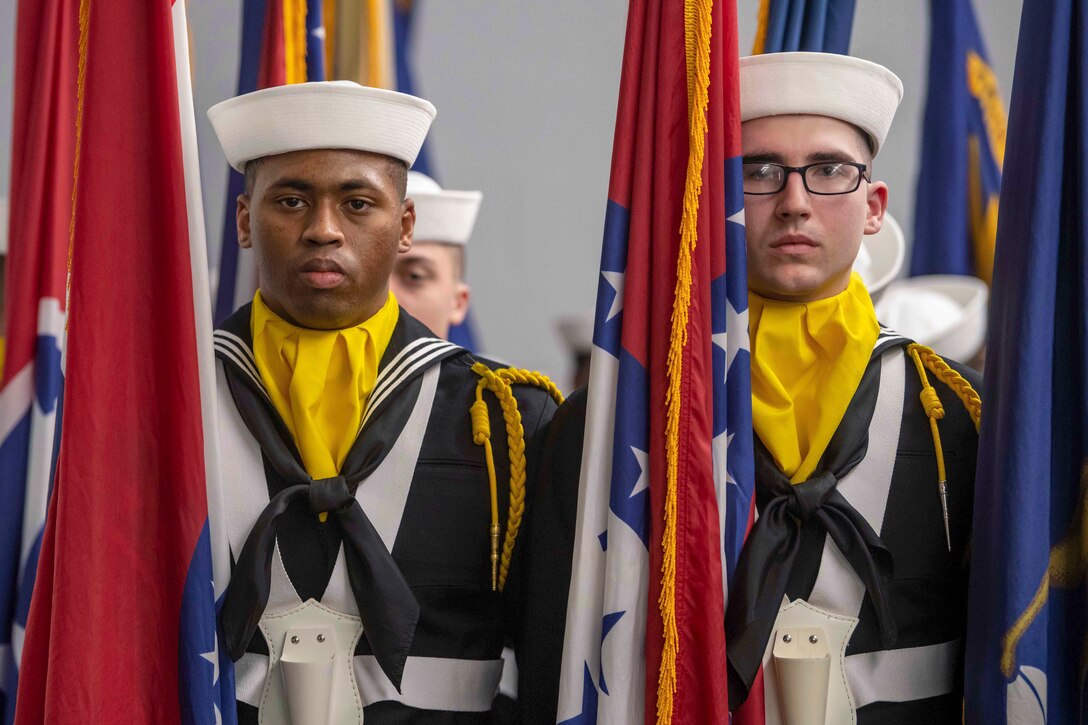 Sailors stand in formation while holding flags.