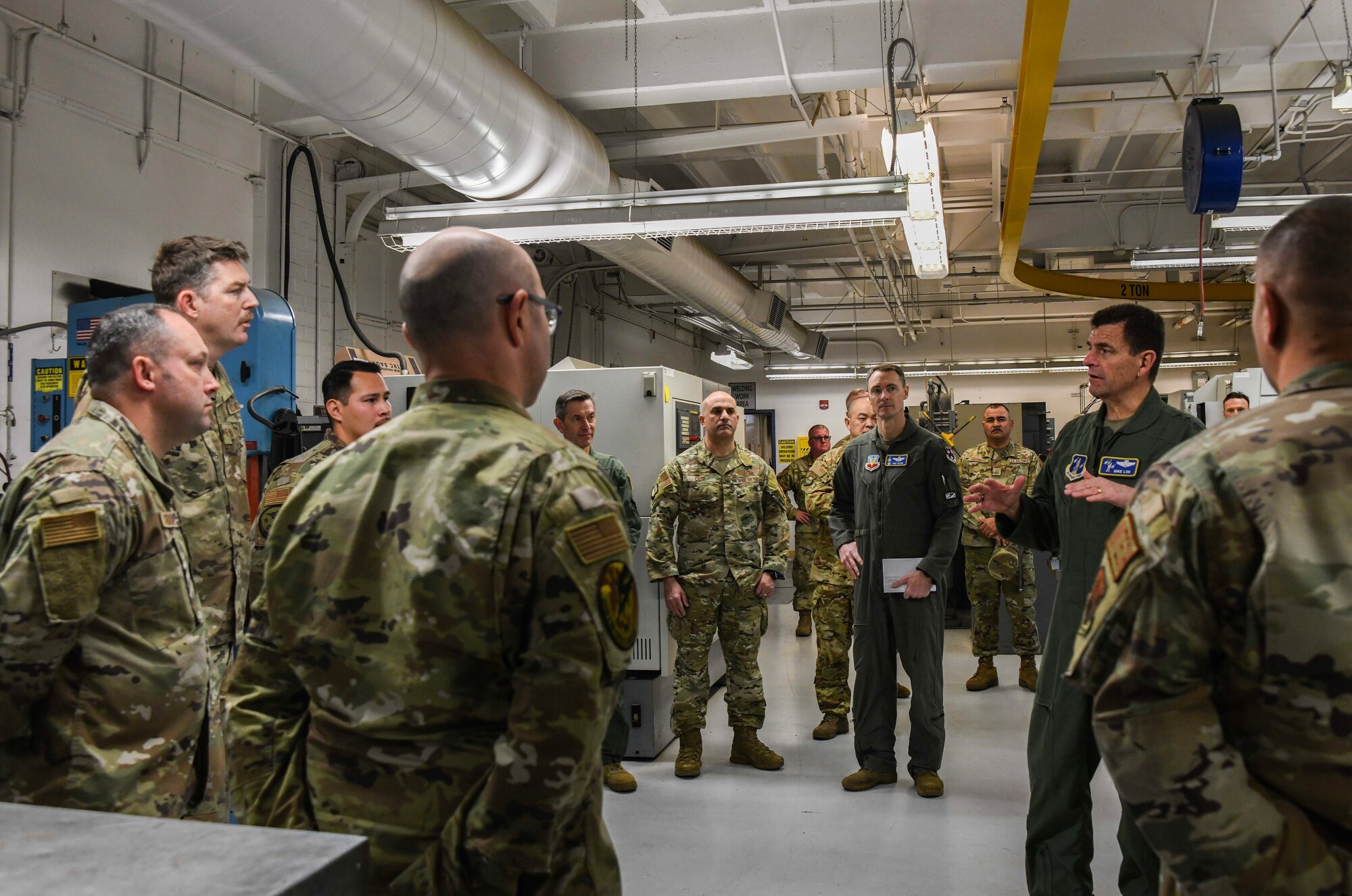 A man in a green flightsuit stands in the middle of a circle of men wearing military camouflage uniforms