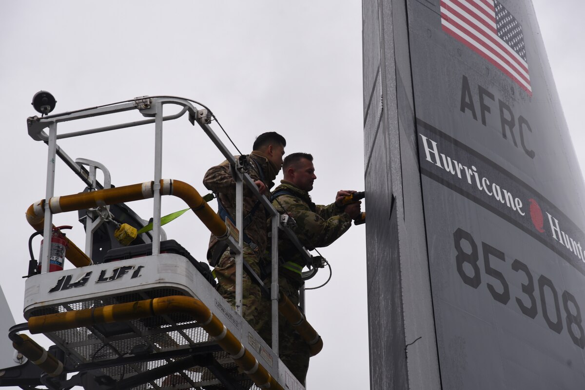 Two male Airmen change a part in the tail of the WC-130J aircraft.