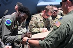 U.S. Air Force Senior Airman Jenson Kokou, left, a boom operator assigned to the 92nd Air Refueling Wing, Fairchild AFB, Washington, and U.S. Air Force Staff Sgt. Nicholas Thurman, a maintainer assigned to the 92nd Aircraft Maintenance Squadron, sign their names on the back of a lithograph in Perth, Australia, Jan. 27, 2023. During each stop of Operation Vespucci, local community members were presented with lithographs to recognize and enhance partnerships with numerous countries in the Southern Hemisphere. (U.S. Air Force photo by 2nd Lt. Kristin Nielsen)