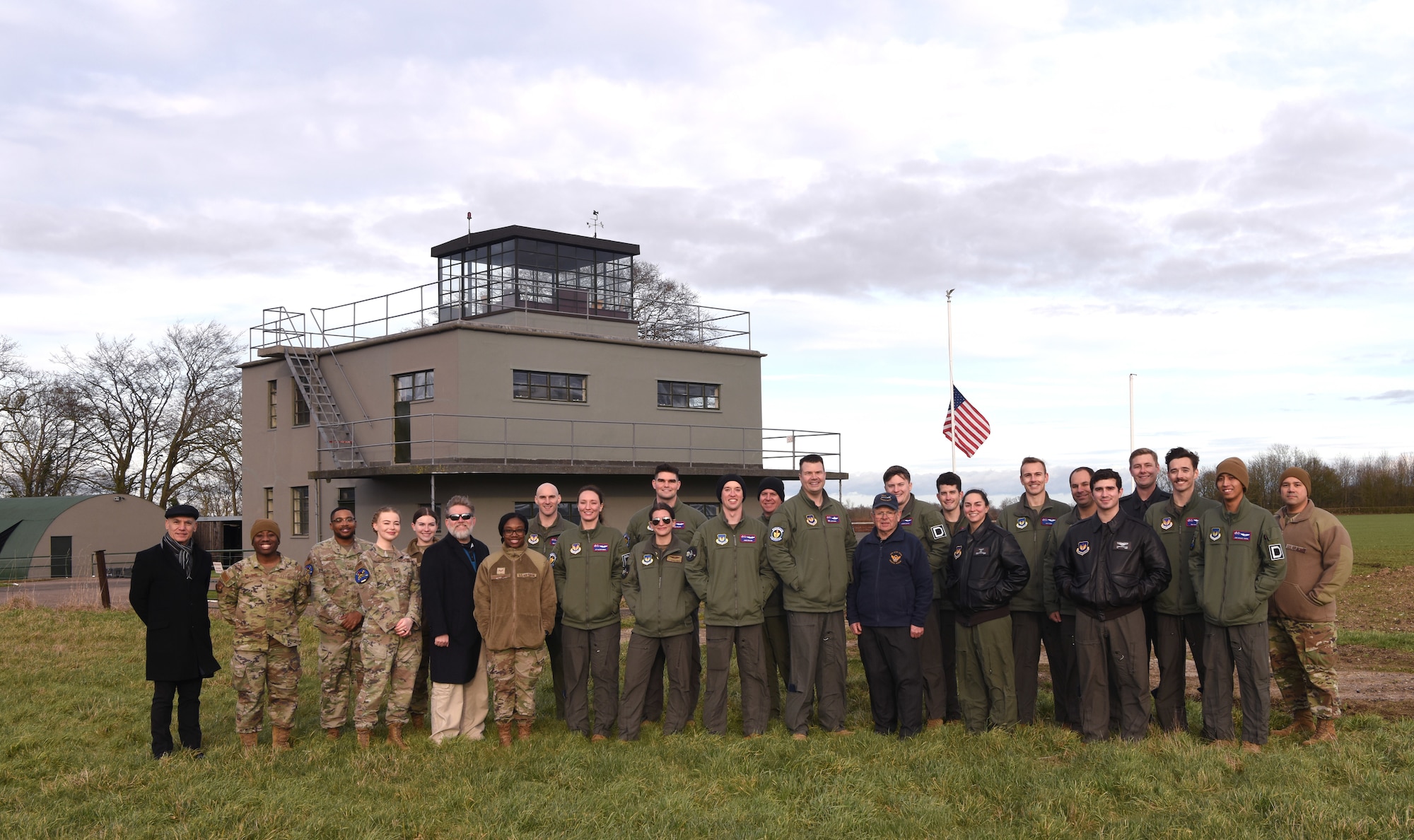 U.S. Air Force Airmen from the 351st Air Refueling Squadron; Rob Paley, 100th Air Refueling Wing historian, and Dr. (Col. ret.) Tom Torkelson, former 100th ARW and 351st ARS commander, gather in front of the air traffic control tower after a patching ceremony at the 100th Bomb Group Memorial Museum, Thorpe Abbotts, England, Feb. 2, 2023. The patching ceremony dates back to World War II and the “Buzzard” patch, presented to pilots and boom operators who have completed mission certification training, is the patch of the 351st Bomb Squadron which flew out of Thorpe Abbotts during World War II. (U.S. Air Force photo by Karen Abeyasekere)