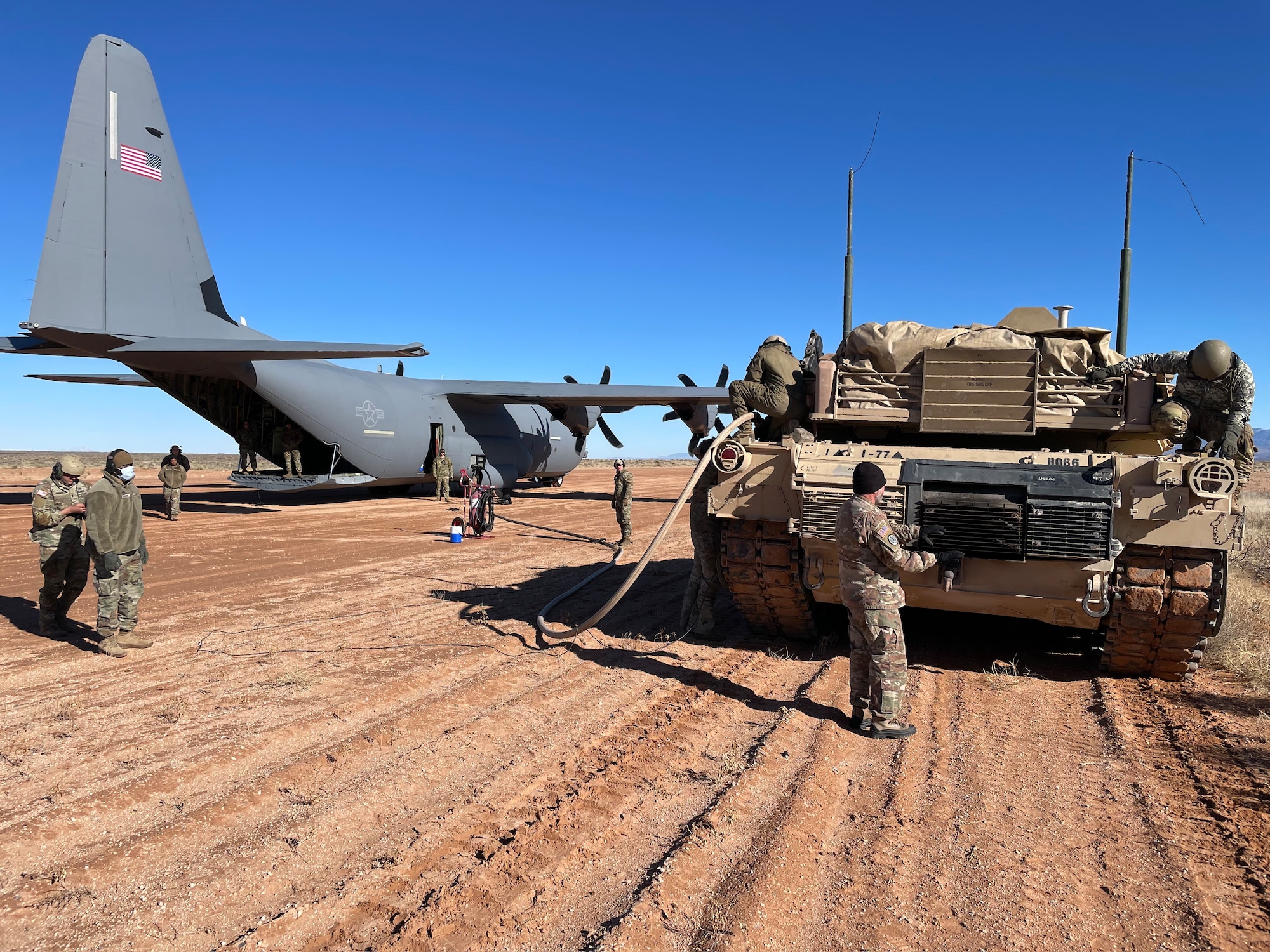 U.S. Air Force Airmen assigned to the 317th Airlift Wing and U.S. Army Soldiers assigned to the 1st Armored Division run a fuel hose from a C-130J Super Hercules to an M1A2 Tank at Fort Bliss, Texas, Jan. 25, 2023. The 317th AW executed an Agile Combat Employment exercise by sending a C-130 to the Fort Bliss Range to perform Specialized Fueling Operations with the 3rd Brigade Combat Team, 1st AD and the 1st Battalion, 77th Armored Regiment. The units successfully passed fuel from a C-130 to an M1A2 Abrams Tank utilizing an Emergency Response Refueling Equipment Kit, marking the first time in Air Force history that a C-130 has been used to refuel an Abrams tank. (Courtesy photo)