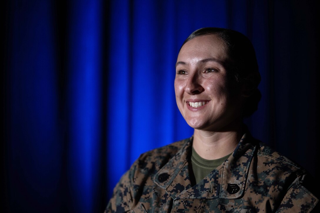 A Marine is shown from the chest up, smiling, in front of a blue curtain.