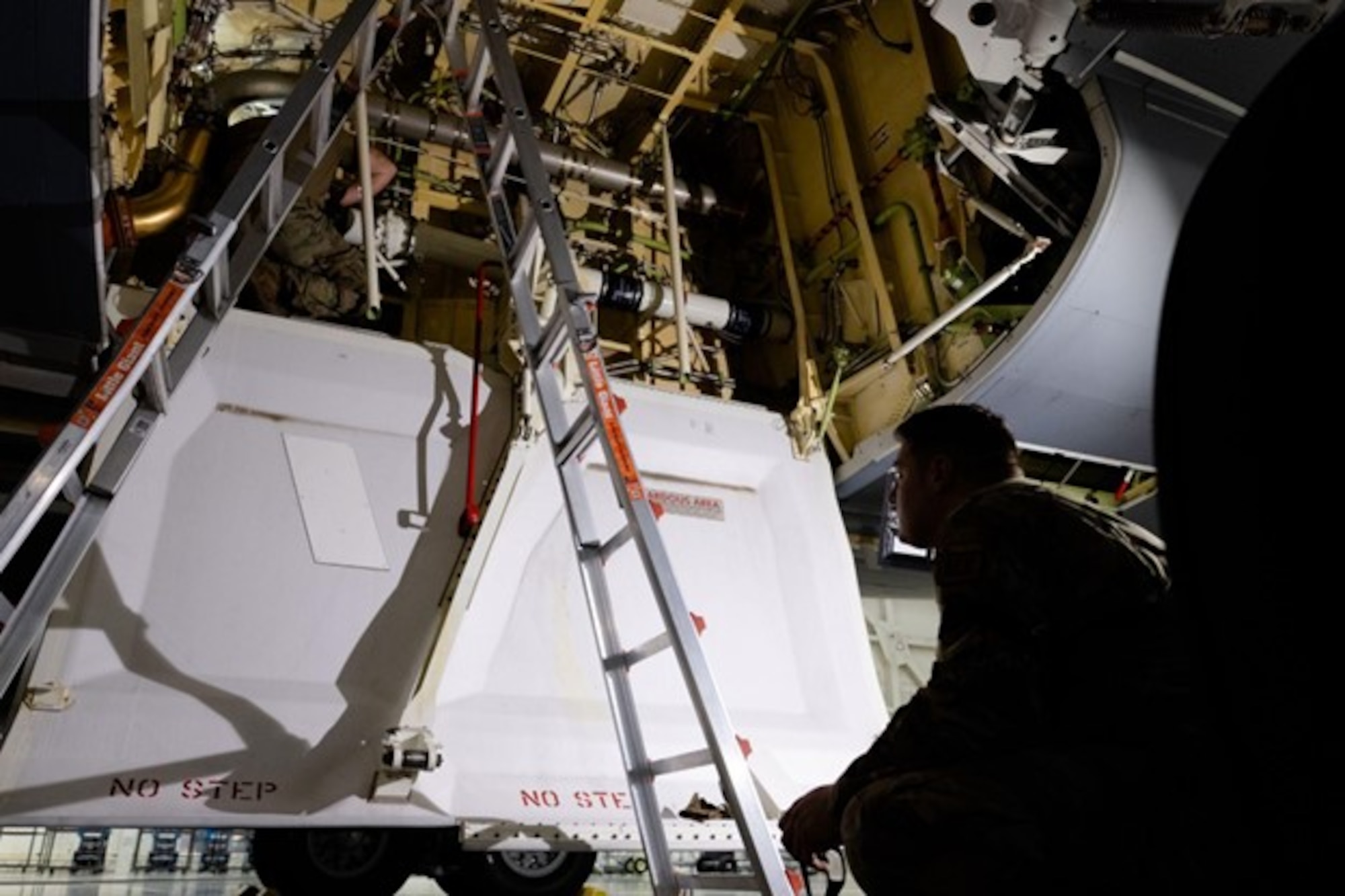 A man crouches as he overlooks another man inside the bay door of a jet