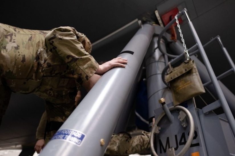 Group of Airmen set up a piece of equipment under a plane