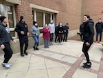 Woman stands in front of group of people, stretching before a run.