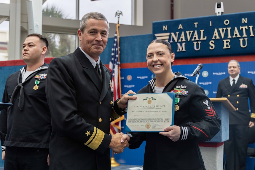 Rear Adm. Pete Garvin, commander, Naval Education and Training Command (NETC), presents a Navy and Marine Corps Commendation Medal to Quartermaster 1st Class Heather Vautard, assigned to Recruit Training Command, Great Lakes, for her selection as the mid-grade enlisted military instructor of the year during the Military Instructor of the Year 2022 awards ceremony at the National Naval Aviation Museum onboard Naval Air Station Pensacola, February 10, 2023. NETC’s mission is to recruit, train and deliver those who serve our nation, taking them from street-to-fleet by transforming civilians into highly skilled, operational and combat ready warfighters. (United States Navy photo by Mass Communication Specialist 2nd Class Zachary Melvin)
