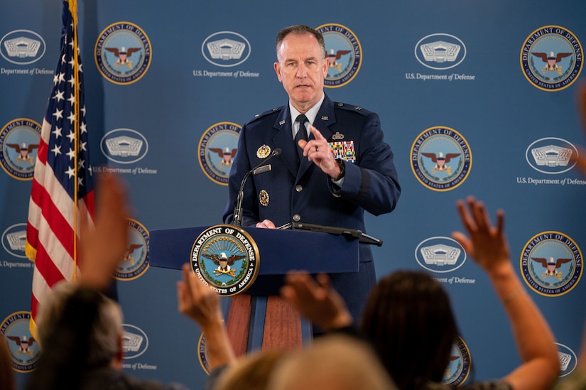 A man in military uniform gestures with his index finger to a crowd of people with their hands raised.