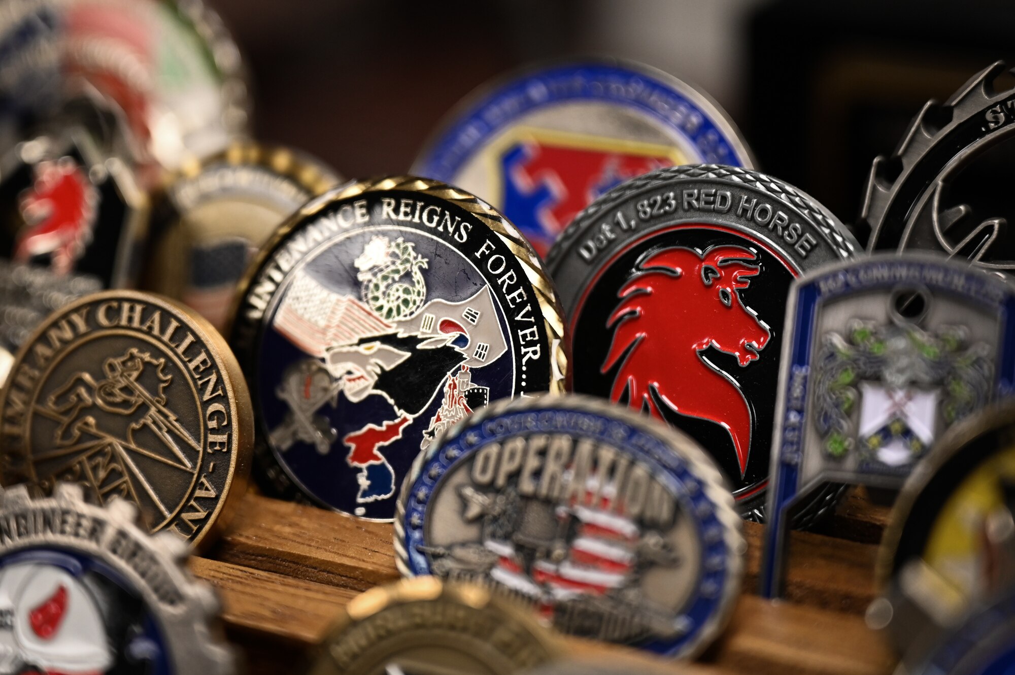 A rack of military challenge coins are displayed on a wooden rack.