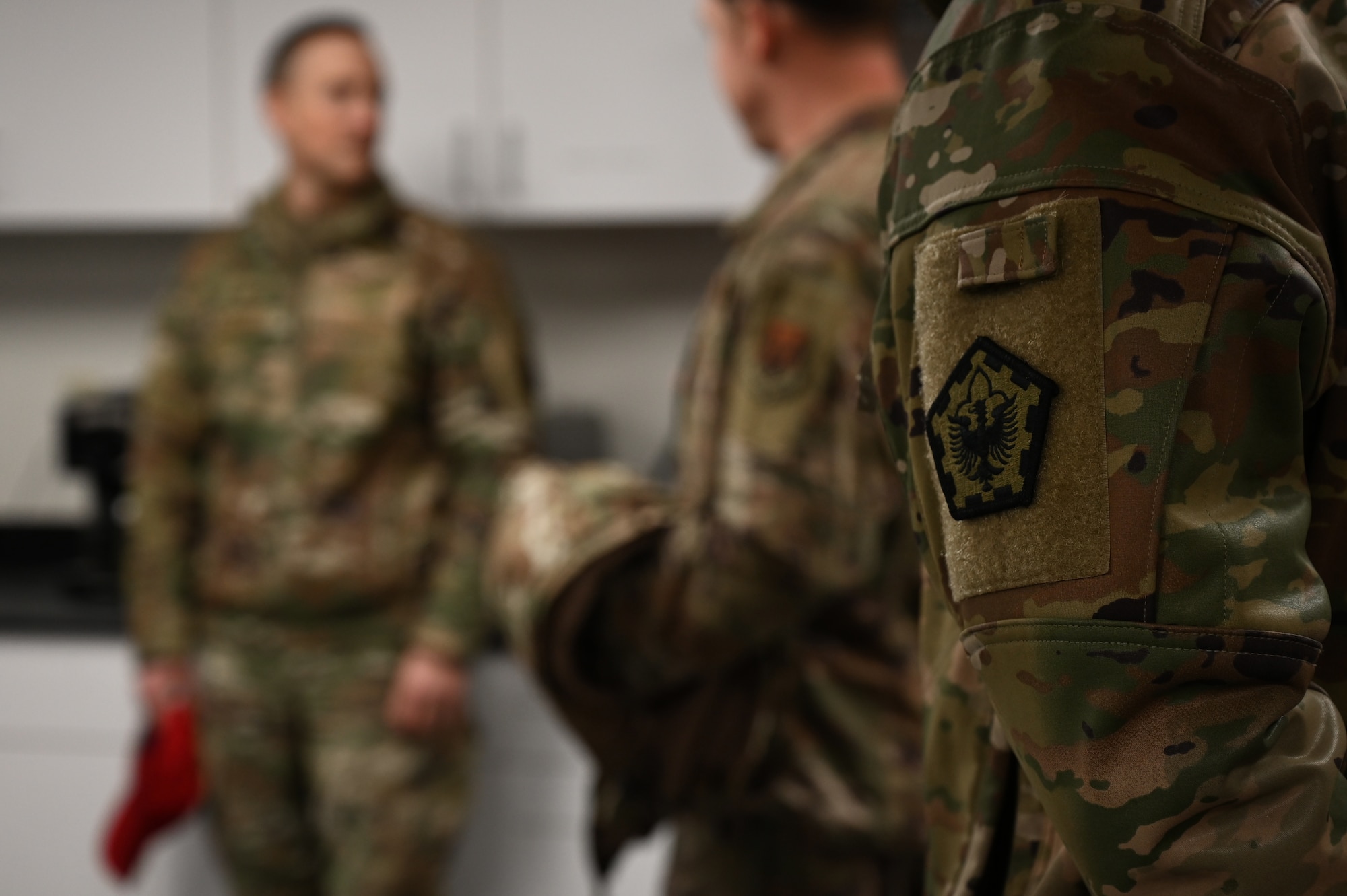 A pentagonal patch with an eagle in the center is worn on the left shoulder of an Airman in uniform.