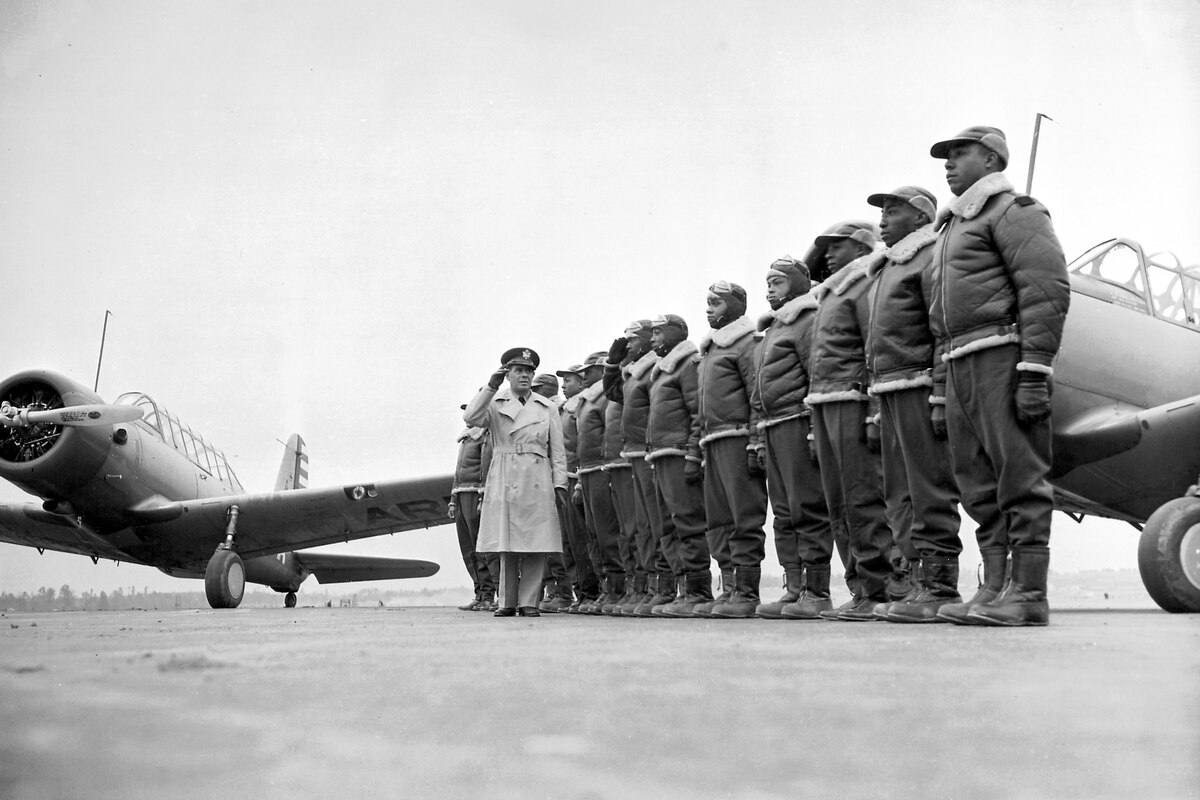Troops stand in formation on a flight line as an officer walks past them and salutes.