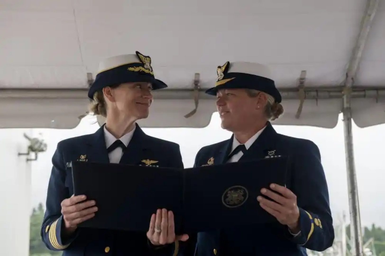 Capt. Breanna Knutson (left), commander Coast Guard Sector North Bend, Oregon, reads an award with Chief Warrant Officer Beth Slade (right) during Coast Guard Station Coos Bay's change of command ceremony in Coos Bay, Oregon, Jun. 10, 2022. Slade was congratulated for her efforts in helping a pregnant member who assisted in the betterment of women's retention in the Coast Guard. (U.S. Coast Guard photo by Petty Officer 3rd Class Diolanda Caballero)