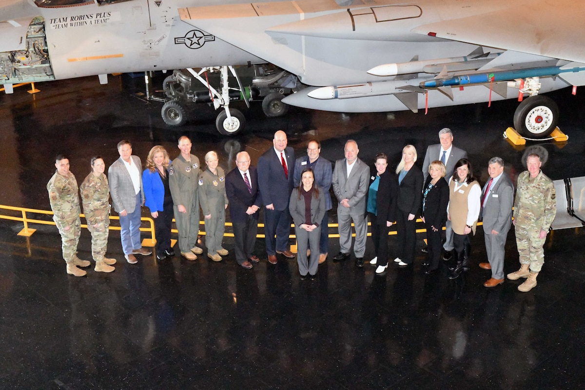 Photo shows a large group standing in front of aircraft display