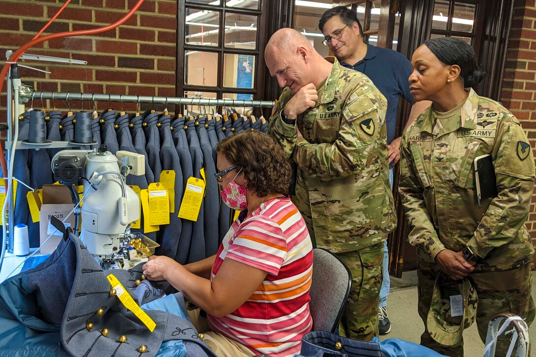 A civilian uses a sewing machine on a uniform as others watch.