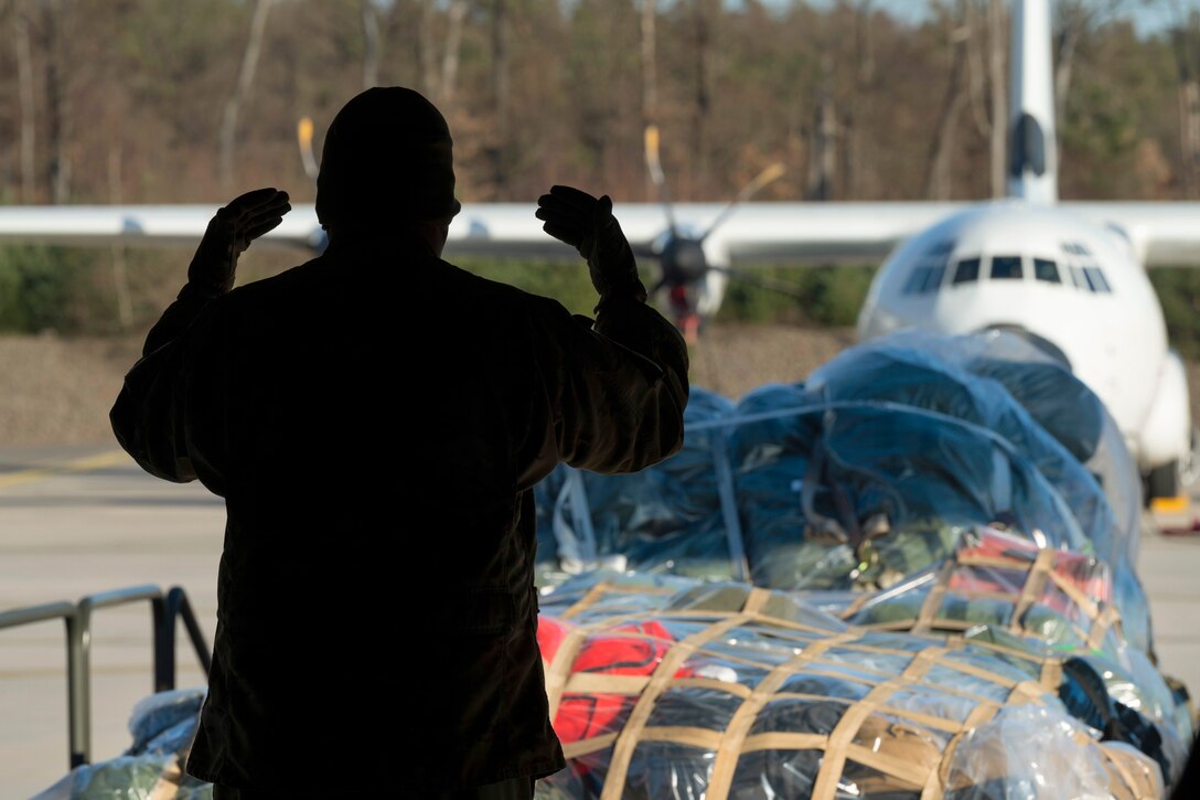 An airman guides a pallet of supplies with an aircraft parked in the background.