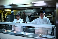 Coast Guard Auxiliary members Joseph Woodbury (left) and Patrick Wolcot (right), place a plate of food on the line while Coast Guard Cutter Healy (WAGB 20) operates in Baffin Bay, Oct. 4, 2021.