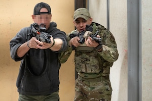 Two individuals, with rifles held at the ready, perform tactical movements