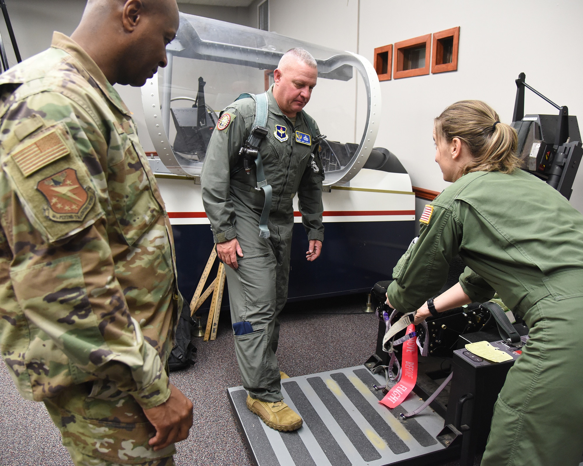 U.S. Air Force Chief Master Sgt. Justin Apticar, center, 19th Air Force command chief, is being instructed by Maj. Rachel Vargas, right, 37th Flying Training Squadron assistant director of operations, on proper use of the ejection seat for a T-6 Texan II, as Chief Master Sgt. Antonio Cooper, 14th Flying Training Wing command chief, looks on at Columbus Air Force Base, Mississippi, Feb. 7, 2023. Apticar and Maj. Gen. Philip A. Stewart, 19th Air Force commander visited Columbus AFB to learn about the Airmen and mission first-hand. (U.S. Air Force Photo by Elizabeth Owens)