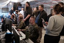 photo of U.S. Air Force military members work on computers in a tent while civilians stand and watch