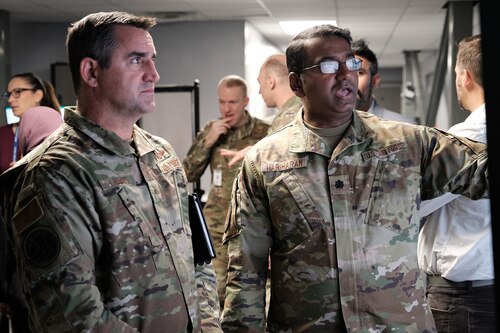 Photo of U.S. Air Force military member briefs general while others work on computers around them