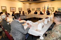 Photo shows group of people sitting around large group of tables speaking to one another
