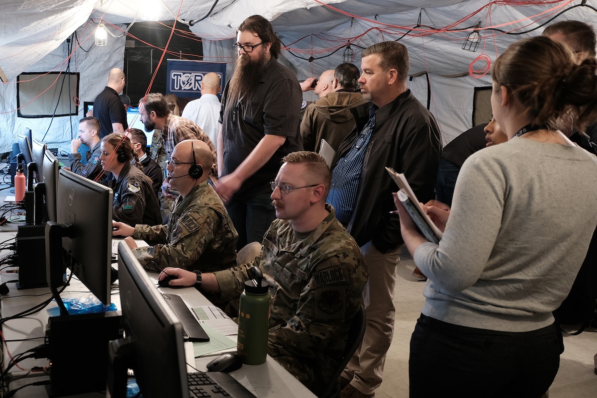 photo of U.S. Air Force military members work on computers in a tent while civilians stand and watch