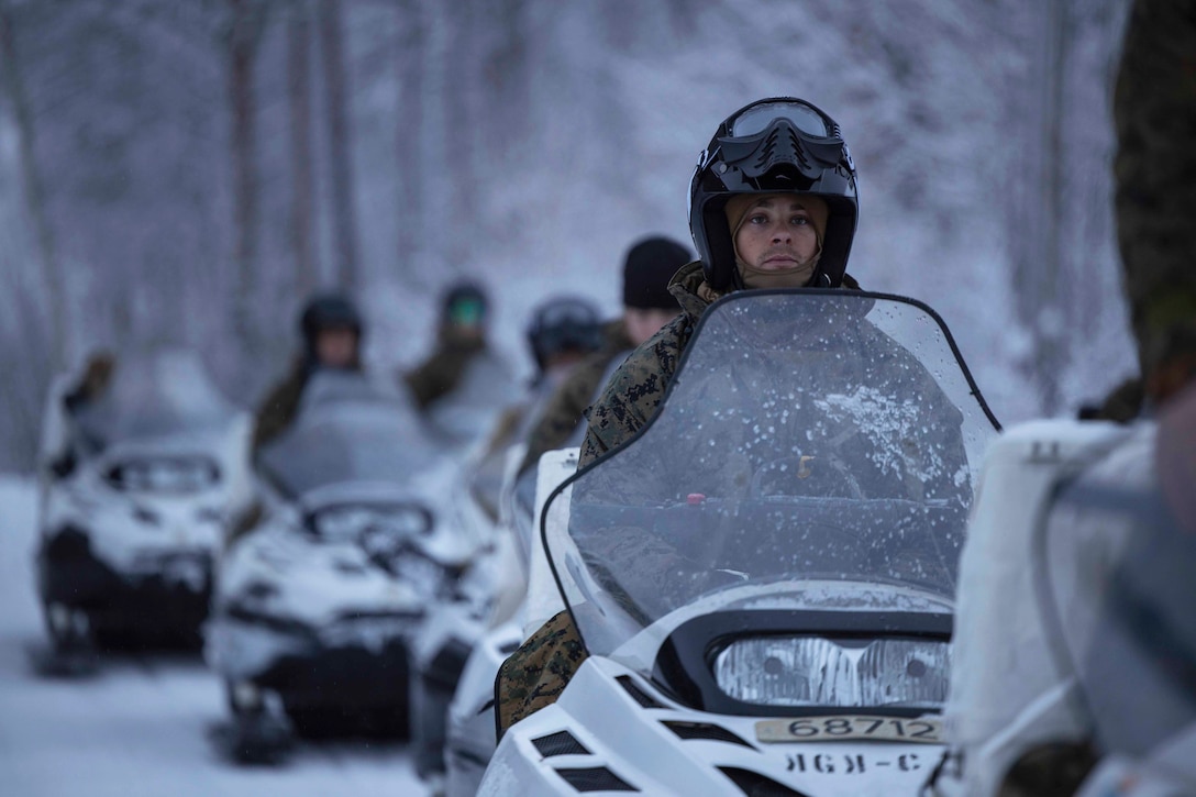 Marines lined up on snowmobiles participate in a training exercise.