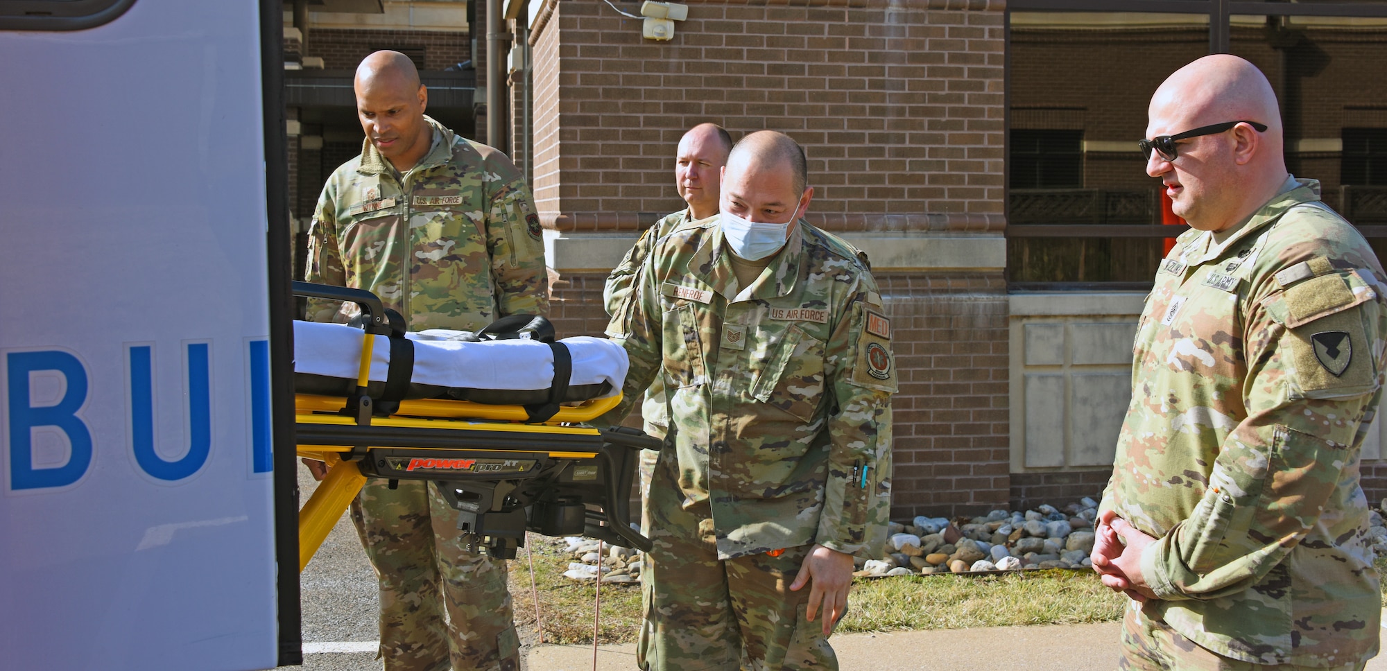 Joint Base MDL leadership watches a paramedic pulling out a wheeled stretcher.