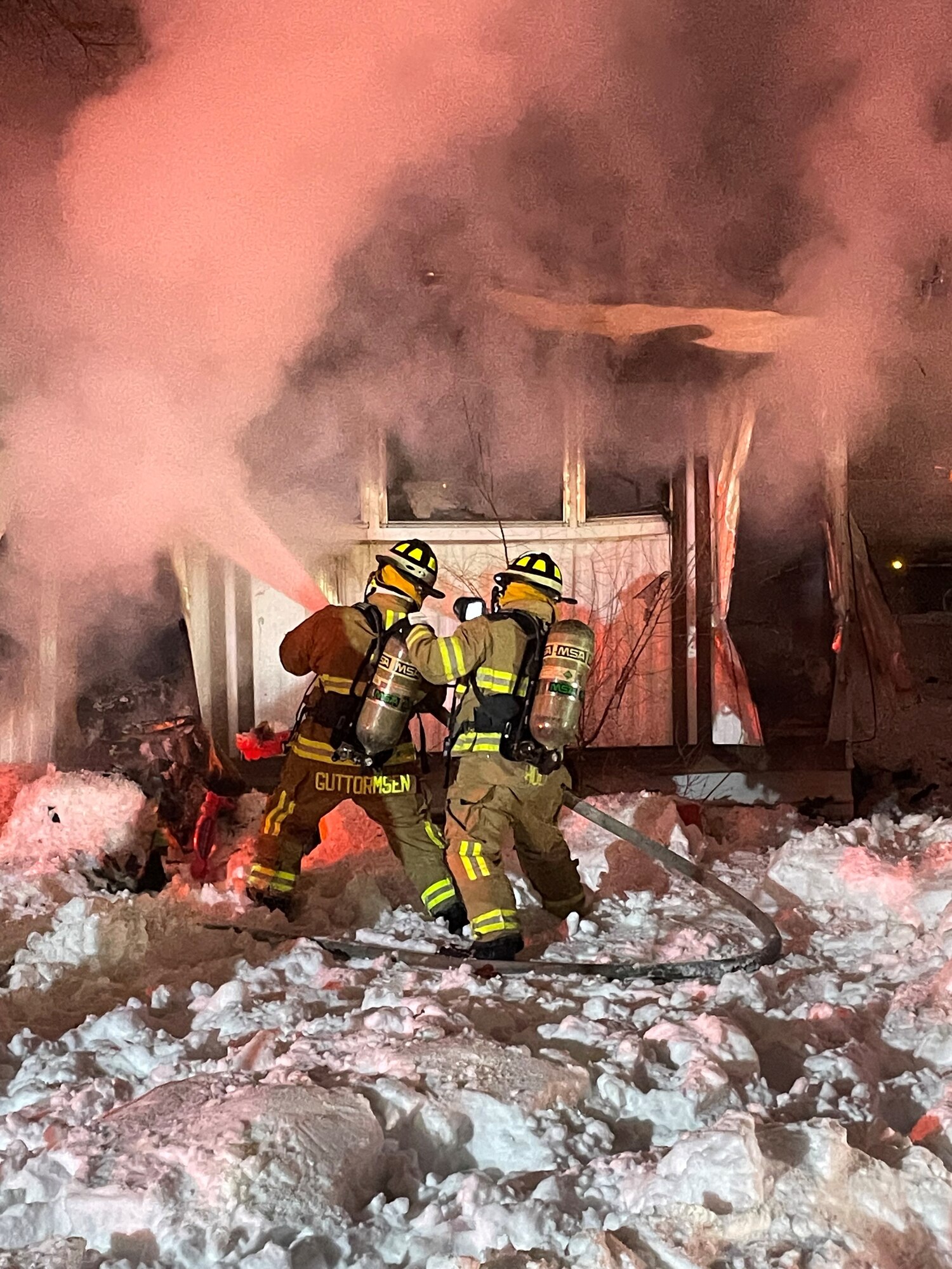 Firefighters use water hose to extinguish burning trailer.