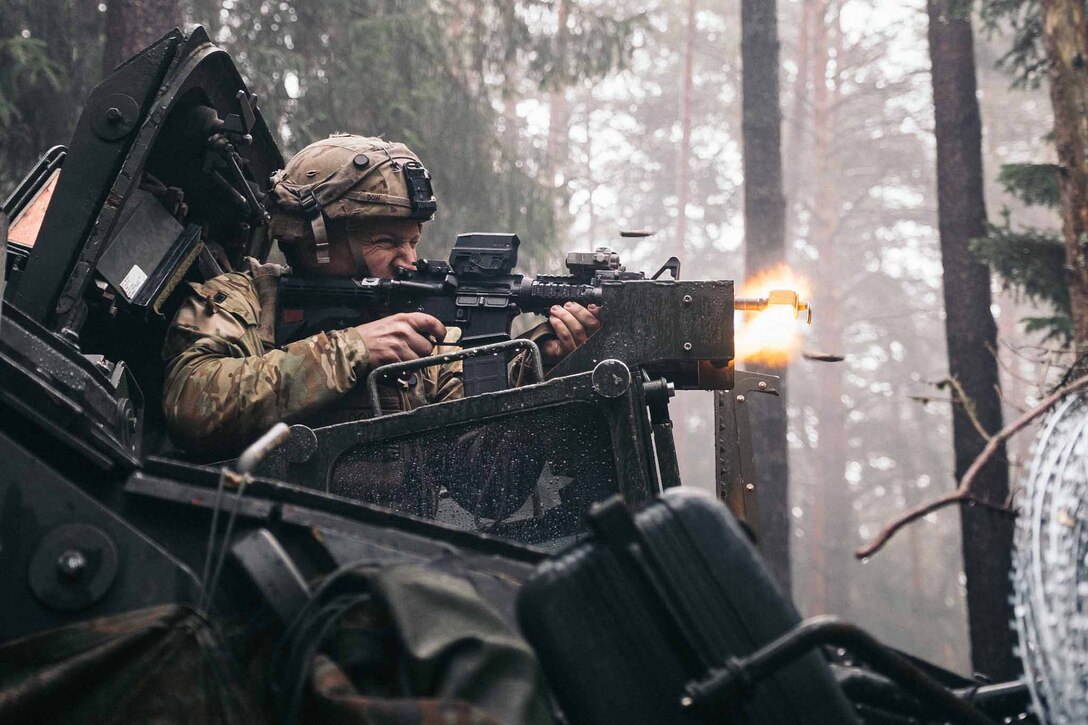 A soldier fires his weapon from inside a vehicle.