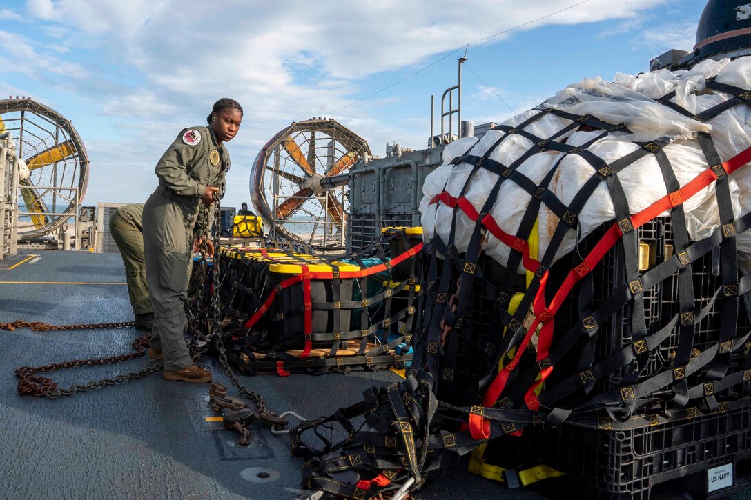A sailor examines a pallet containing parts of a  balloon on a ship.